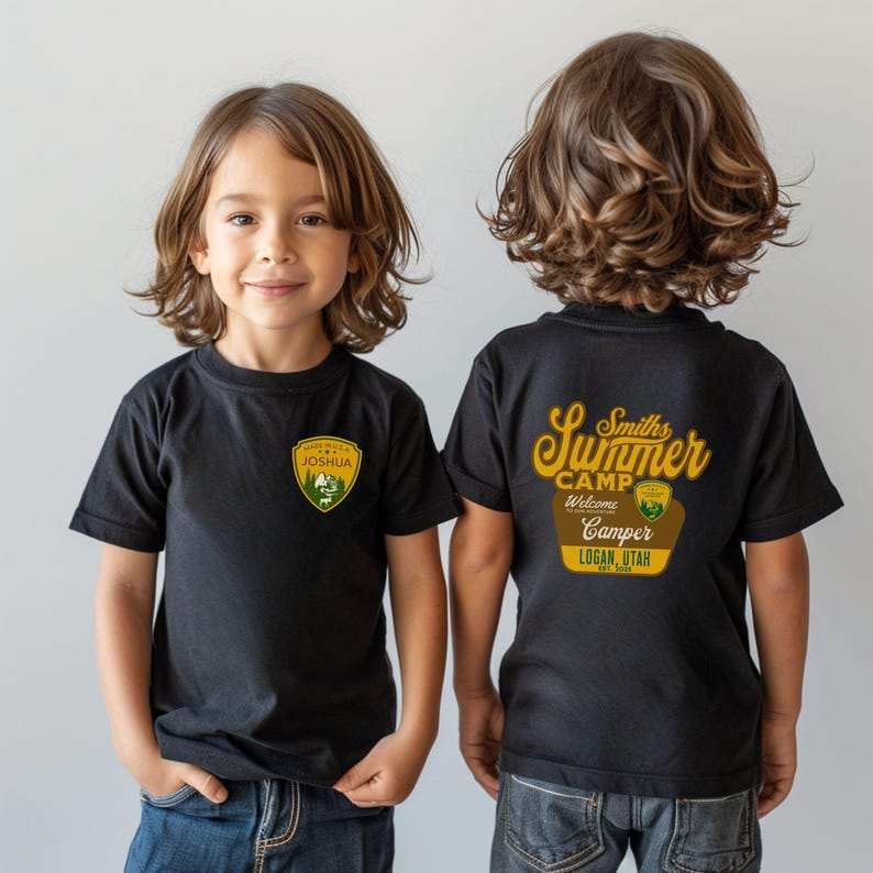 May include: Two black t-shirts with a camping theme. The front of one shirt has a yellow patch with the text "Made in the USA Joshua" and a green mountain scene. The back of the other shirt has a yellow and brown graphic with the text "Smiths Summer Camp Welcome Camper Logan, Utah Est. 2020".
