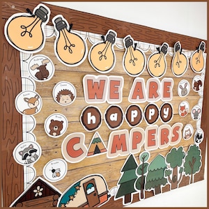 Op de afbeelding: Houten prikbord met de woorden "WE ARE HAPPY CAMPERS" in oranje en witte letters. Het bord is versierd met gloeilampuitsparingen, dierenillustraties en een campertrailer-afbeelding. Het algemene thema is kamperen.