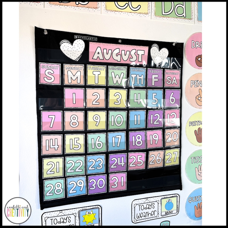 May include: A black calendar with a white heart and the word "AUGUST" in pink letters. The calendar has pockets for each day of the month, with colourful numbers in each pocket. The calendar is hanging on a white wall.