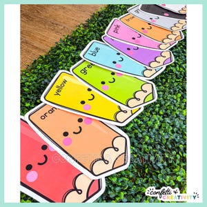 May include: A set of colorful pencil-shaped cards featuring cute faces with pink cheeks and black eyes. Each card is labeled with its corresponding color name, including red, orange, yellow, green, blue, purple, pink, brown, gray, and black.