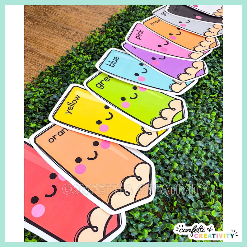 May include: A set of colorful pencil-shaped cards featuring cute faces with pink cheeks and black eyes. Each card is labeled with its corresponding color name, including red, orange, yellow, green, blue, purple, pink, brown, gray, and black.
