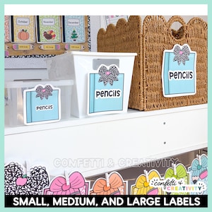 May include: Three storage containers featuring light blue rectangular labels with a black and white speckled bow graphic and the text pencils. The labels are attached to a small clear bin, a medium white bin, and a large woven brown basket.