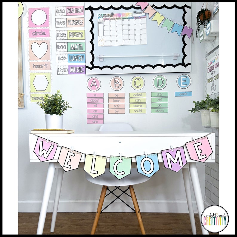 May include: A colourful welcome banner with pastel-coloured letters, each letter is a different colour and has a glitter-like texture. The banner is hanging from a white desk with a white chair. The banner is made of cardstock and has a scalloped edge.