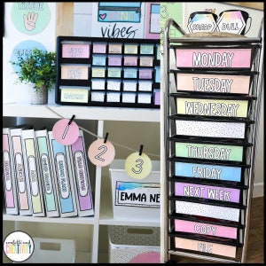 May include: A black metal rolling cart with colourful drawers labelled with the days of the week, Monday through Friday, and "Next Week" and "Copy File". The cart is in a classroom setting with a white shelf unit behind it. The shelf unit has binders labelled with subjects such as "Reading", "Science", "Data", "Guided Reading", "Lesson Plans", and "Team Meetings".