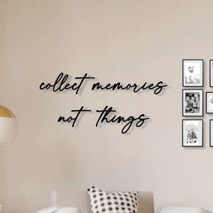 Op de afbeelding: Een woonkamer met een witte bank en een zwart-wit geruit kussen. De muur is beige en heeft een zwart kalligrafie-citaat met de tekst "collect memories not things". Er hangen 12 zwarte fotolijsten aan de muur met zwart-wit foto's.