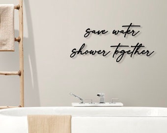 May include: White bathtub with a towel hanging on the side. The wall behind the tub has a black script that reads "save water shower together".