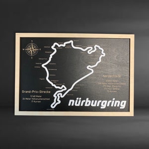 May include: A wooden plaque with a white outline of the N&uuml;rburgring race track. The plaque features the text "Nordschleife" and details about the track, including its length, elevation change, and number of turns. The text "Grand-Prix-Strecke" and details about the track are also included.