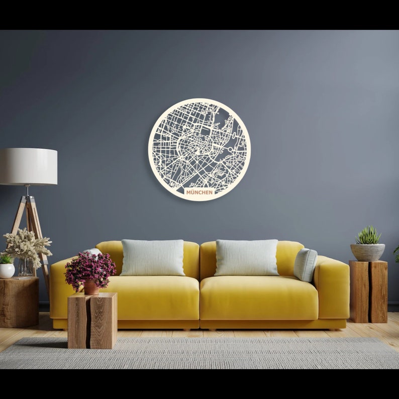 May include: A white wooden circle with a detailed map of Munich, Germany, cut out. The circle is hanging on a gray wall above a yellow couch. The text "MUNCHEN" is printed below the circle.