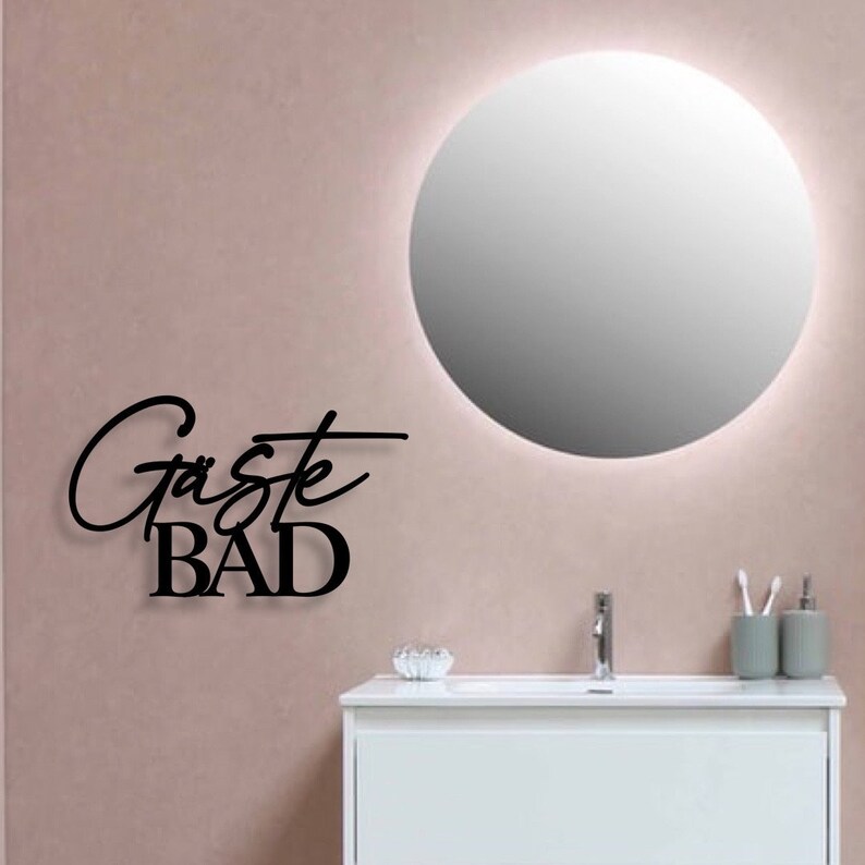 May include: A bathroom with a round mirror, a white sink, and a black metal sign that says "G&auml;ste BAD".
