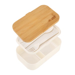 May include: White lunchbox with a removable bamboo cutting board lid. The lunchbox has a built-in compartment for cutlery and a separate compartment for food. The lid has the text "Lunchbox" printed on it.