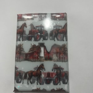 May include: A white light switch cover with a red barn, brown horses, and red tractors on a white background.