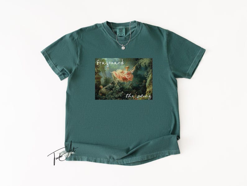 May include: Teal-colored t-shirt featuring a framed print of Fragonard's "The Swing" painting. The text "Fragonard" and "the swing" are printed below the image. A silver necklace with a small pendant is visible.