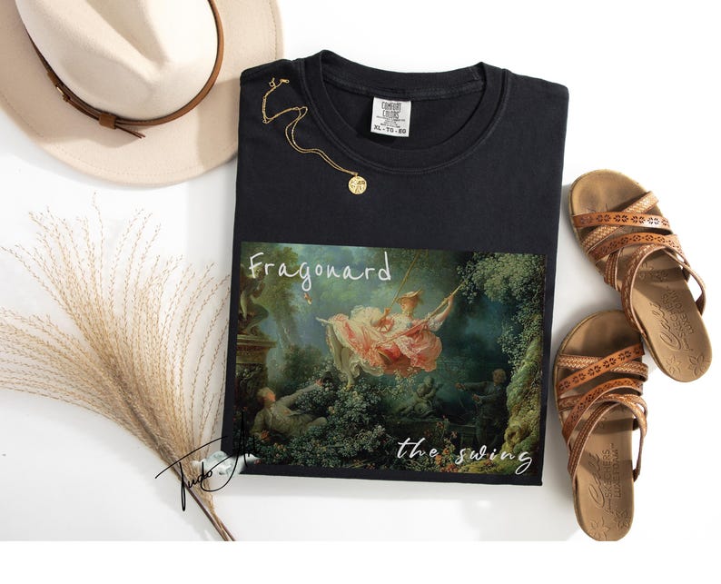 May include: Black t-shirt featuring a print of Fragonard's "The Swing" painting. The shirt is styled with a gold necklace, brown sandals, and a beige hat. A bundle of dried ornamental grass is also included.