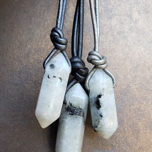 May include: Three white crystal pendants with black inclusions, each hanging from a leather cord. The cords are tied together in a knot at the top.
