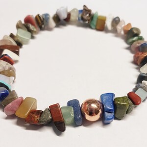 May include: A colorful bracelet made of assorted gemstone chips and a single copper-colored bead. The gemstones are various shapes and sizes, including red, blue, green, and brown. The bracelet is strung on an elastic band.