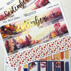 May include: A sticker sheet set featuring an autumn sunset landscape with watercolor trees in shades of orange, red, and purple. The text September is printed in gold foil. Includes day-of-the-week labels, fall leaf patterns, and various rectangular boxes.