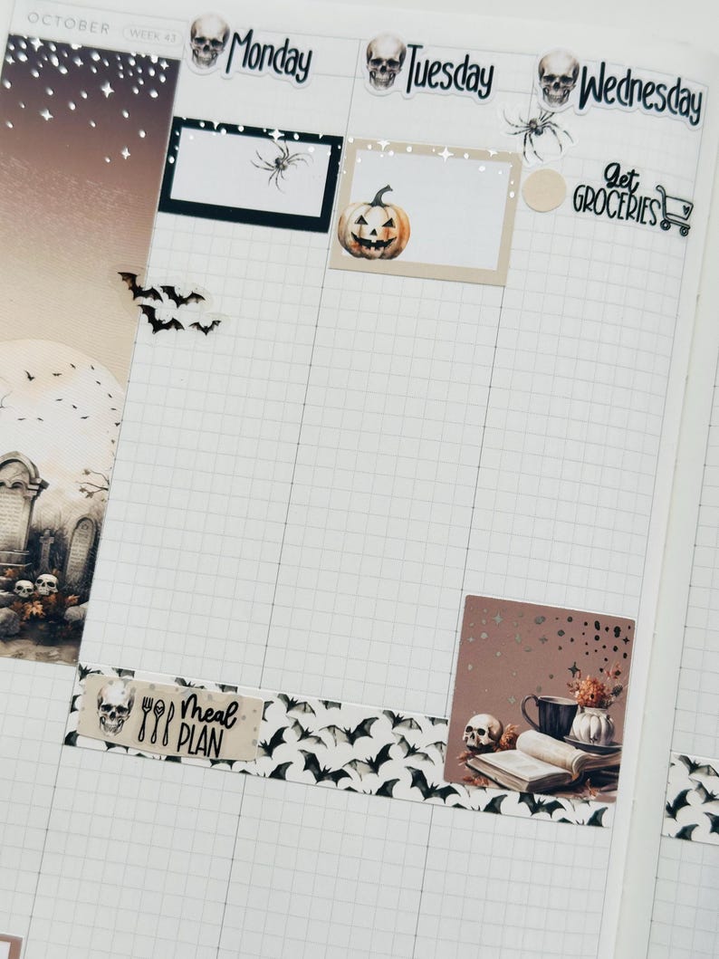 May include: A weekly planner with a Halloween theme. The planner has a grid layout with days of the week labeled: Monday, Tuesday, Wednesday. The planner has a variety of stickers, including a pumpkin, a skull, a spider, bats, and a "Get Groceries" sticker with a shopping cart icon. The planner also has a "Meal Plan" sticker with a skull and cutlery.