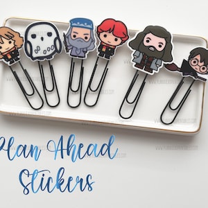 May include: Six Harry Potter themed paper clips with different characters from the series. The characters include Harry Potter, Hermione Granger, Ron Weasley, Dumbledore, Hedwig, and Hagrid. The paper clips are black and have a white background. The text "Plan Ahead Stickers" is written in blue below the paper clips.
