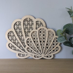 May include: Two wooden seashell wall decorations with intricate cut-out designs. The larger seashell has a fan-shaped pattern, while the smaller seashell has a woven pattern.