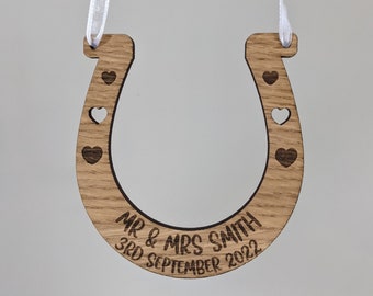 May include: Wooden horseshoe ornament with a white ribbon for hanging. It is engraved with "Mr & Mrs Smith 3rd September 2022" and has small hearts carved into the horseshoe.