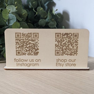 May include: A wooden sign with two QR codes. The left QR code has the text "follow us on Instagram" below it. The right QR code has the text "shop our Etsy store" below it.