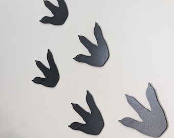 May include: Five black dinosaur footprints cutouts on a white wall. The footprints are arranged in a random pattern.