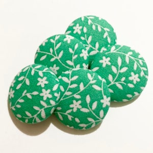 May include: Five green fabric buttons with a white floral pattern. The buttons are round and have a slightly raised surface.