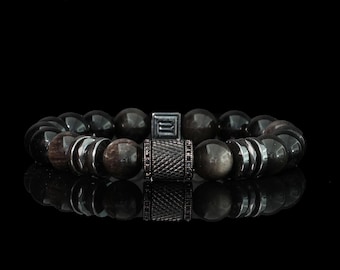 May include: A black beaded bracelet with a central cylindrical bead and a square bead. The bracelet features a mix of dark, round beads and metallic accents. The beads are approximately 0.5 inches in diameter.