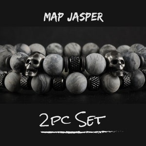 May include: Two gray stone bracelets with black metal skull beads and black metal spacers. The bracelets are stacked on top of each other. The text "MAP JASPER 2PC SET" is written in white on a black background.