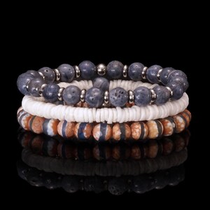 May include: Three stacked bracelets with different bead designs. The top bracelet features dark blue, round beads with silver accents. The middle bracelet has white, shell-like beads. The bottom bracelet has brown and blue patterned beads.