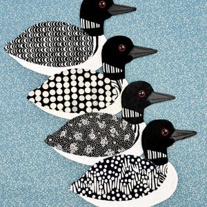 May include: Four decorative loon figures with black heads, necks, and beaks, and white bodies with various black patterns. The loons are arranged diagonally on a light blue background with a floral pattern.