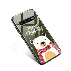 Puede incluir: Una funda transparente para teléfono con fondo verde y un oso polar blanco que lleva una bufanda roja y blanca. El texto "Merry Christmas" está escrito en blanco en la funda.