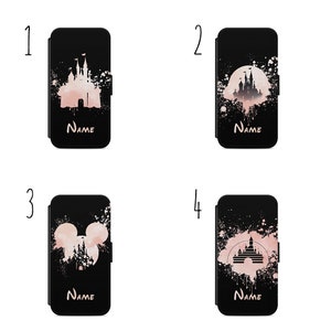 Op de afbeelding: Vier verschillende telefoonhoesjes met een zwarte achtergrond en roze waterverfspatten. De hoesjes hebben verschillende Disney-kasteel silhouetten. De tekst "NAME" is op elk hoesje gedrukt.