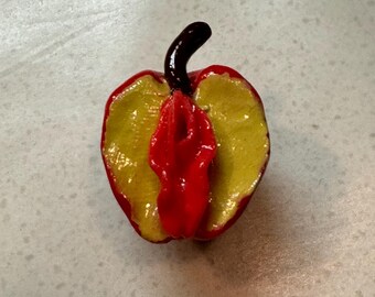 Puede incluir: Figurita de manzana estilizada y artesanal. La manzana presenta un exterior rojo vibrante con un interior amarillo y un tallo marrón oscuro. El diseño es una representación artística única de una manzana.