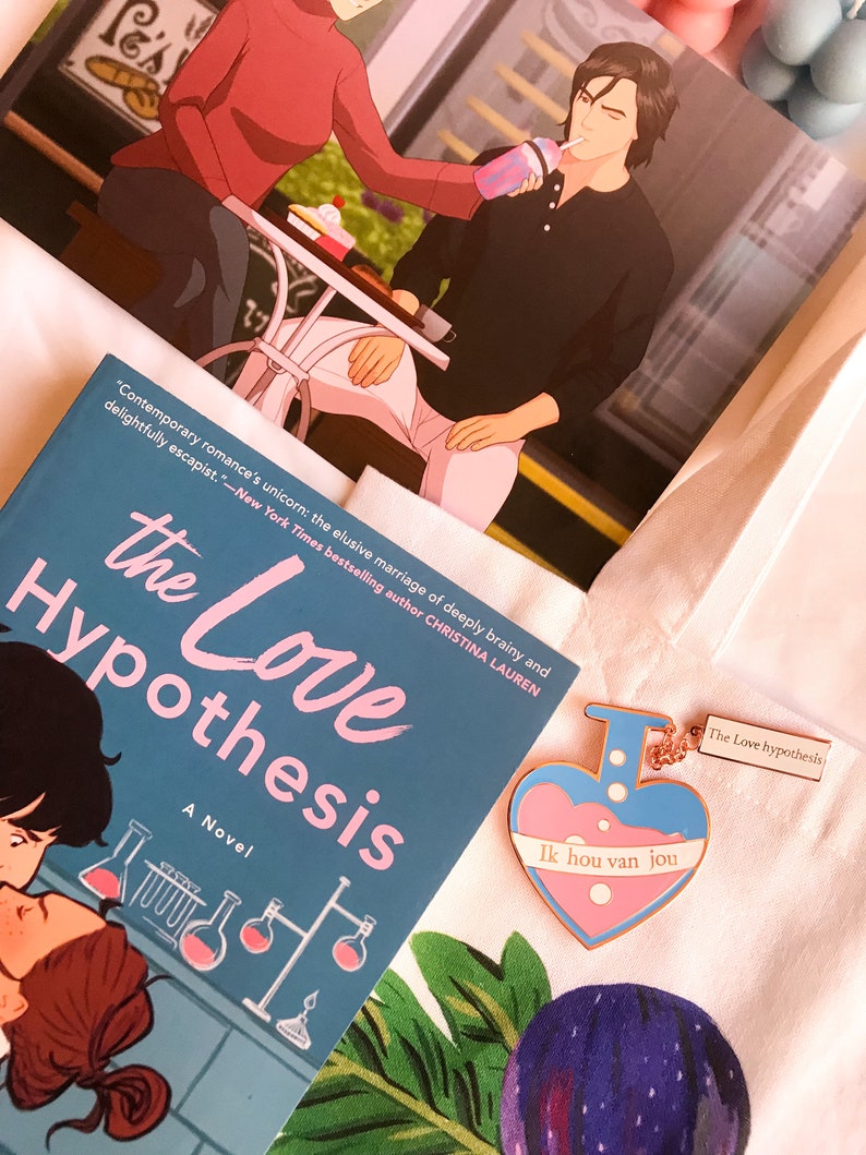 May include: A novel titled "The Love Hypothesis" with a teal cover and illustrations of lab equipment. A heart-shaped enamel pin with the text "Ik hou van jou" and a print of a couple are also visible.