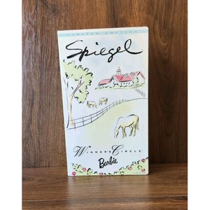 Puede incluir: Una caja blanca con un dibujo de una granja con un techo rojo y caballos en un campo. La caja dice "Spiegel" y "Winner's Circle Barbie" en cursiva.