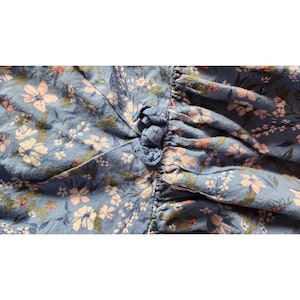 Puede incluir: Una tela azul con un patr&oacute;n floral en tonos de rosa y blanco. La tela tiene un detalle fruncido en la parte superior.