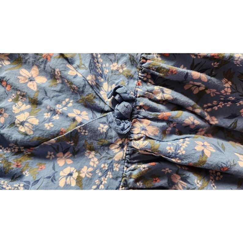 Puede incluir: Una tela azul con un patr&oacute;n floral en tonos de rosa y blanco. La tela tiene un detalle fruncido en la parte superior.