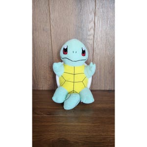 May include: A plush toy of Squirtle, a Pokemon character. The toy is blue and green with a yellow shell. It has big eyes and a friendly expression.