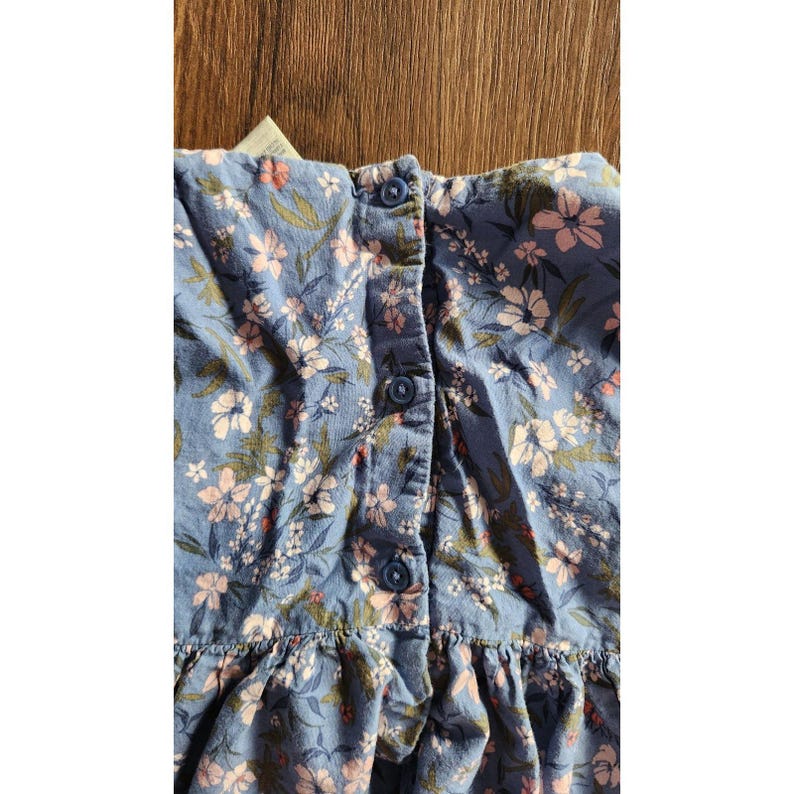 Puede incluir: Un vestido azul y blanco con estampado floral, con botones en la parte delantera y un dobladillo con volantes.