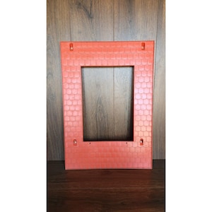 May include: Orange plastic roof section for a dollhouse or playhouse. The roof has a brick pattern and is designed to be attached to the walls of a structure.