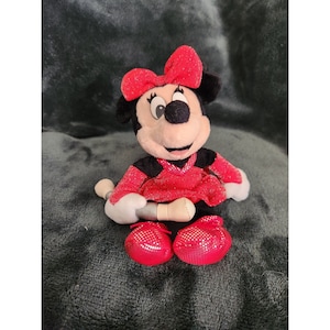 May include: A red and black plush toy of Minnie Mouse wearing a red sparkly dress and a red bow. She is holding a silver microphone.