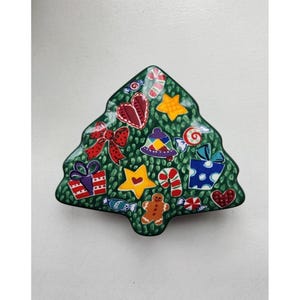 Puede incluir: Una caja de cerámica verde en forma de árbol de Navidad con una variedad de decoraciones navideñas coloridas pintadas en ella, incluyendo regalos, bastones de caramelo, estrellas y un hombre de jengibre.
