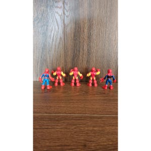 May include: Five colorful superhero action figures. The figures include Spider-Man and Iron Man characters. The figures are red, blue, and yellow. The figures are standing on a wooden surface.