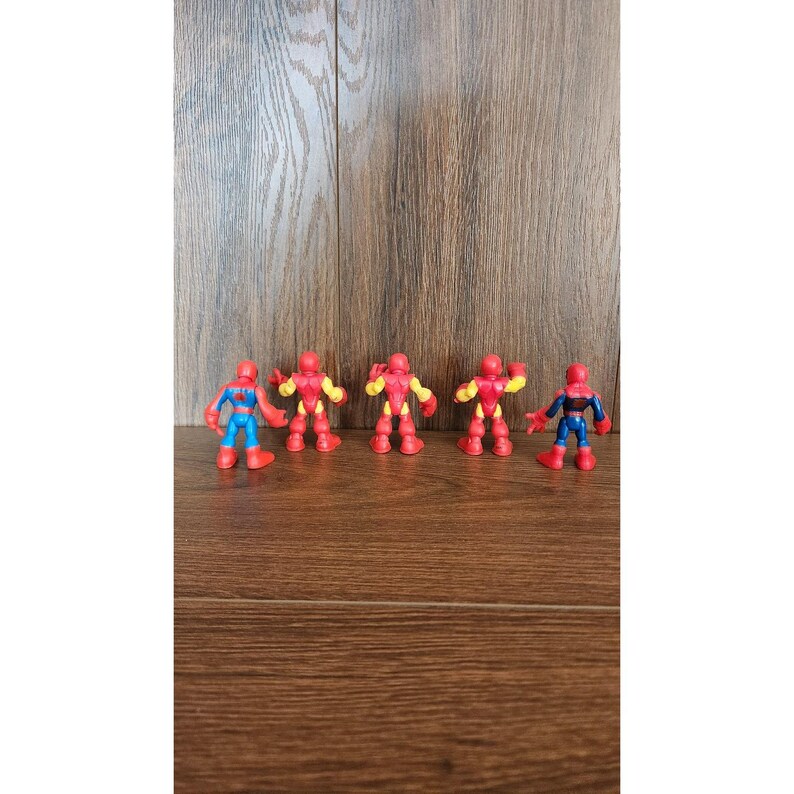 May include: Five colorful superhero action figures. The figures include Spider-Man and Iron Man characters. The figures are red, blue, and yellow. The figures are standing on a wooden surface.