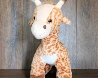 Könnte beinhalten: Ein Giraffen-Plüschtier mit beigefarbenem und braunem Fleckenmuster, einer cremefarbenen Schnauze und einem weißen Fleck auf der Brust. Das Stofftier hat zwei kleine Hornzapfen auf dem Kopf, dunkelbraune Hufe und schwarze Kunststoffaugen.