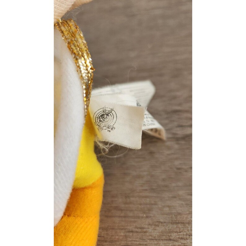 May include: A yellow and white plush toy with a gold trim and a white tag that says "Made in China" on it.