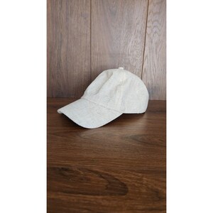May include: A light beige baseball cap made of a textured fabric. The cap has a curved brim and a slightly rounded crown.