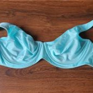 May include: A bright turquoise underwire bra featuring molded cups, adjustable shoulder straps, and a hook-and-eye closure at the back. The garment includes a small white brand tag attached to the side strap, showcasing a smooth fabric finish.