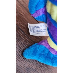 May include: A blue, purple, and yellow plush toy with a tag that reads "Great American Toy Co., Inc. All New Materials Consisting of: Polyester Fibers & PVC Pellets. Made in PA-5793 (RC), Ohio. For Ages 4 and Up. 3"